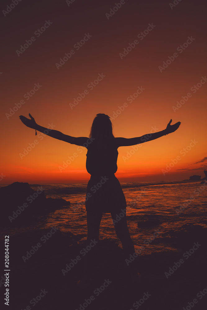 Girl with arms wide open enjoying sea / ocean scenery in sunset.