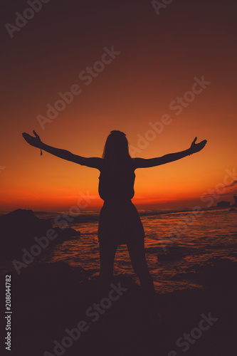 Girl with arms wide open enjoying sea / ocean scenery in sunset.