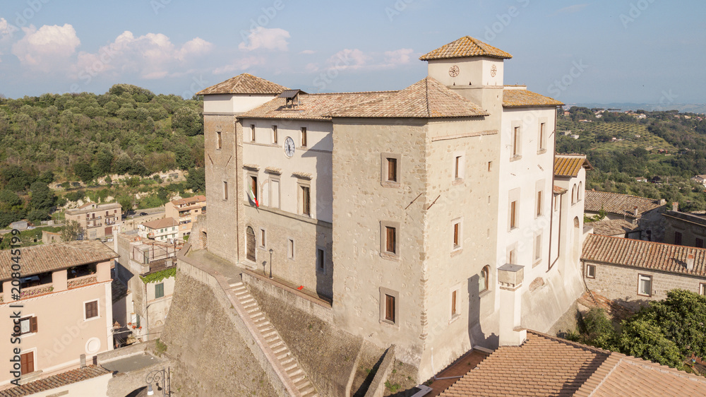 Aerial view of Castelnuovo di Porto castle, near Rome in Italy. The building has a square shape with four towers at the corners. On the facade there is a clock and around the houses of the village.