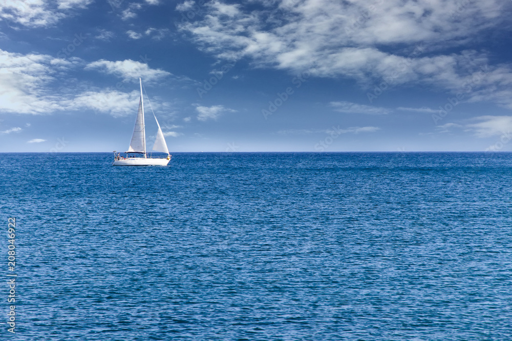 Fototapeta premium White modern yacht sailboat sailing alone on calm blue sea waters on a beautiful sunny day with blue sky and white clouds.