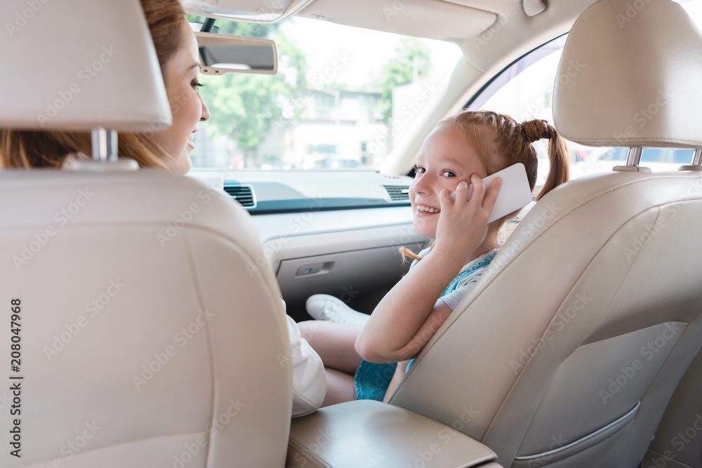 side view of smiling kid talking on smartphone with mother near by in car side view of smiling kid talking on smartphone with mother near by in car