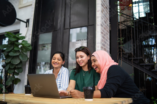 a group of woman chatting and laughing at cafe with a laptop in front