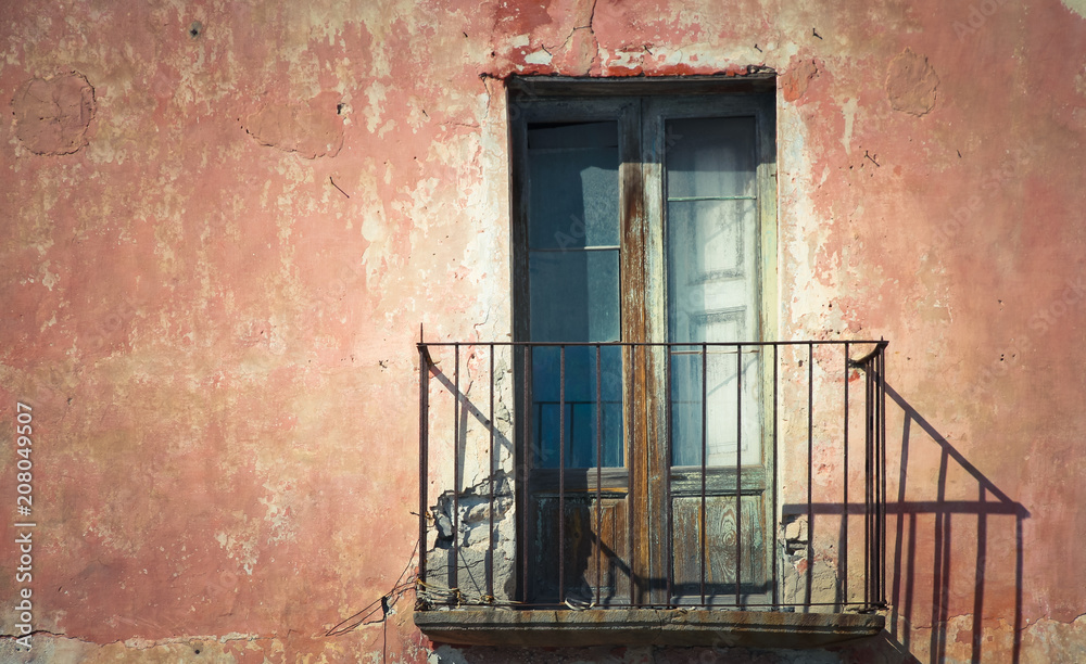 Obraz premium Rustic old grungy and weathered wooden closed door of rusty balcony with a red brown vintage cracked wall with peeling paint in a Southern Italy house typical facade.