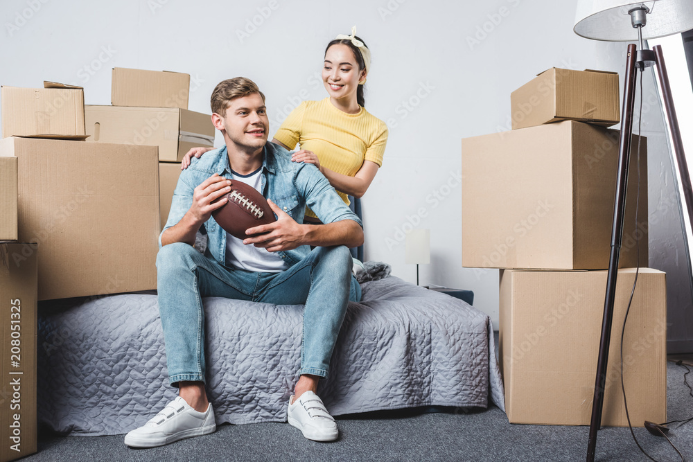 beautiful young couple sitting in bedroom of new home with american football ball beautiful young couple sitting in bedroom of new home with american football ball