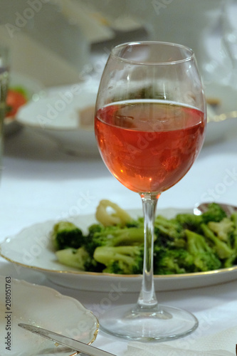 Vertical picture. A glass of pink wine on a table next to a broccoli salad.