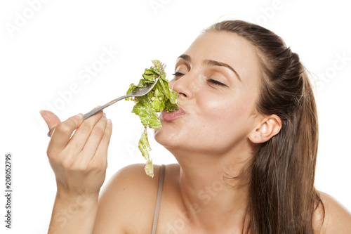 young happy woman eating lettuce salad on a white background