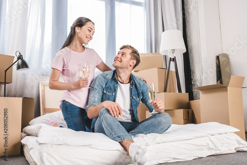 beautiful young couple sitting on bed with champagne while moving into new home