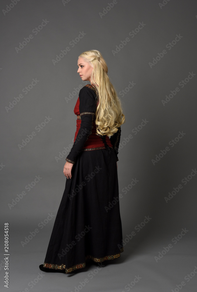 full length portrait of pretty blonde lady wearing a red and black fantasy medieval gown. standing pose on grey background. full length portrait of pretty blonde lady wearing a red and black fantasy medieval gown. standing pose on grey background.
