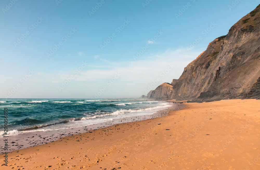 A deserted beach with volcanic cliff and the blue green waters of the Atlantic Ocean in Sagres, Algarves, Portugal during Summer.
