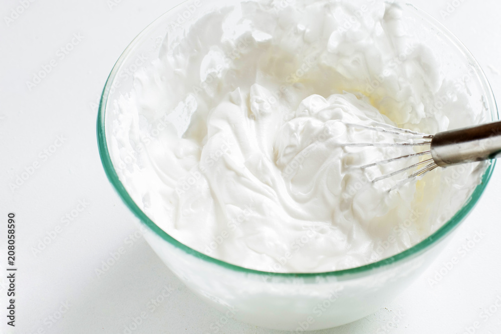 Whipped eggs in a bowl with a whisk on a white table