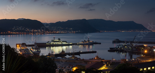 The lights on a ship in harbour reflect in the calm water at sunset