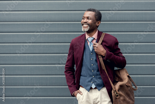 happy stylish african american man in burgundy jacket with leather bag photo