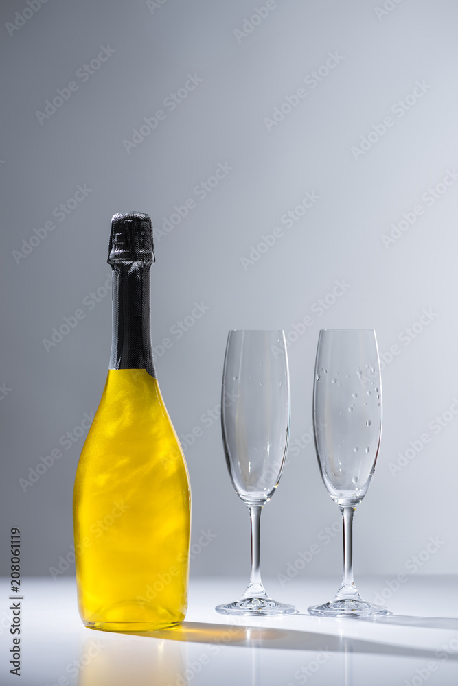 close up view of bottle of champagne and empty glasses on grey background close up view of bottle of champagne and empty glasses on grey background