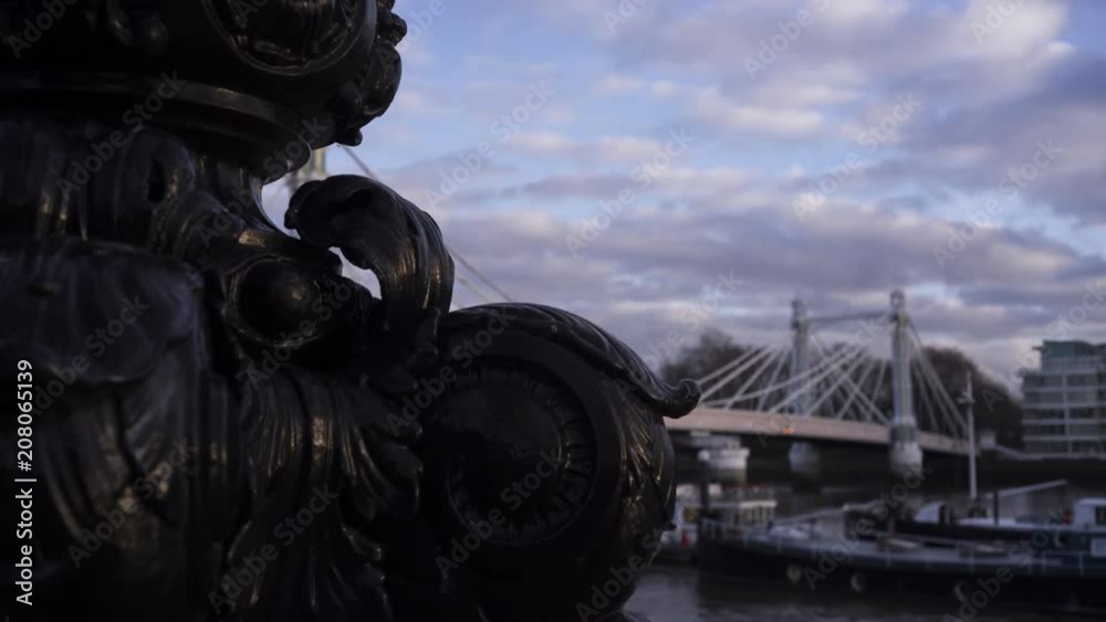 Timelapse of Albert Bridge with boats moored in Thames River, bronze sculpture in foreground, Chelsea, London, United Kingdom Timelapse of Albert Bridge with boats moored in Thames River, bronze sculpture in foreground, Chelsea, London, United Kingdom