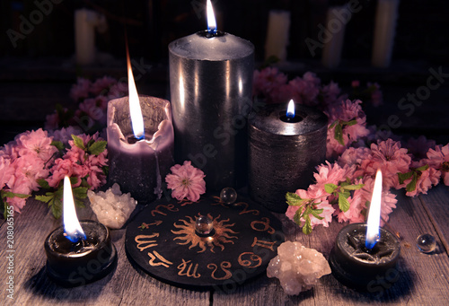 Black candles and zodiac circle with sakura flowers on witch table. Occult, esoteric and divination still life. Halloween background with vintage objects 