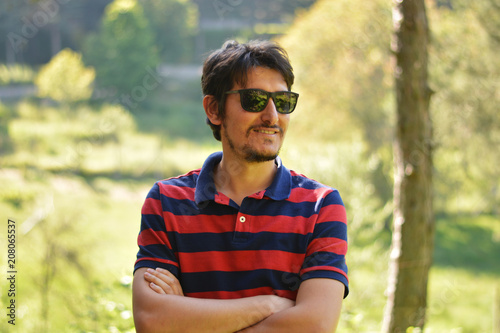 Young man outdoors portrait not looking at the camera with natural green background. Happy Facial Emotion.