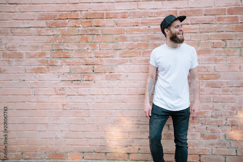 Hipster handsome male model with beard wearing white blank t-shirt and a baseball cap with space for your logo or design in casual urban style