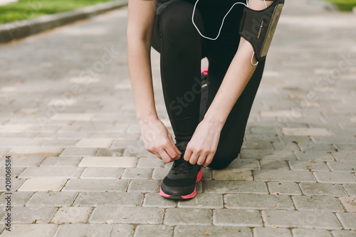Cropped close up of woman hands tying shoelaces on black and pink sneakers on jogging or training on path outdoors. Fitness, healthy lifestyle concept. Copy space for advertisement.