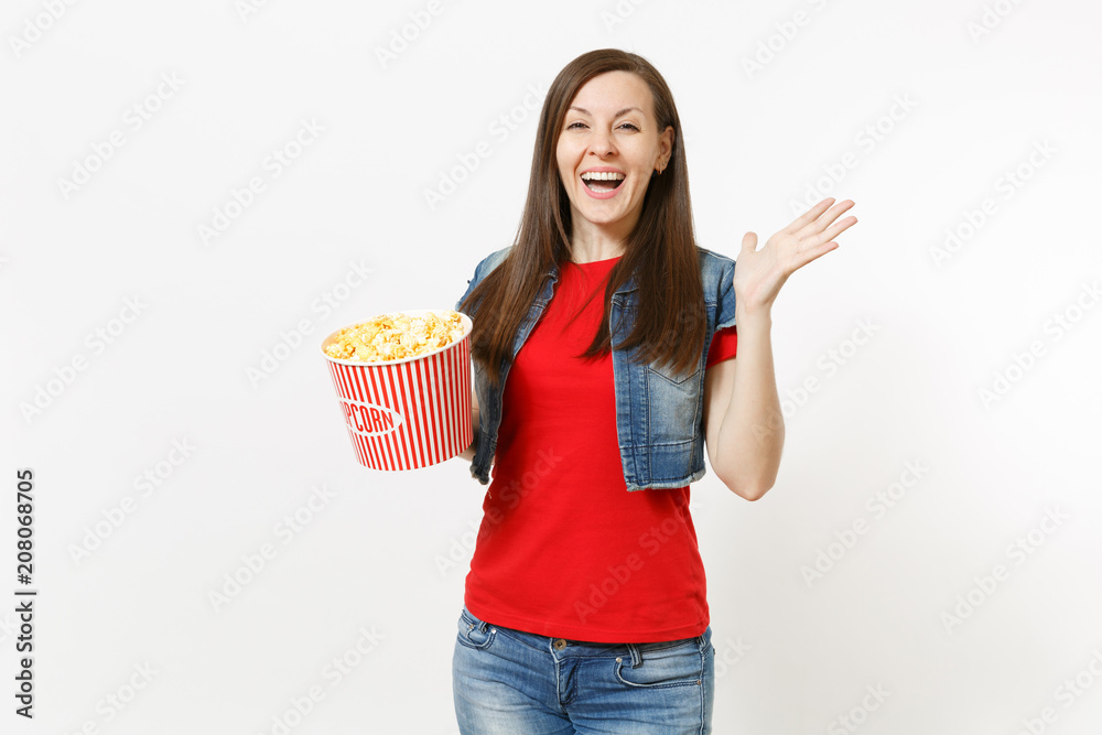 Portrait of young laughing overjoyed beautiful woman in casual clothes watching movie film, holding bucket of popcorn and spreading hand isolated on white background. Emotions in cinema concept. Portrait of young laughing overjoyed beautiful woman in casual clothes watching movie film, holding bucket of popcorn and spreading hand isolated on white background. Emotions in cinema concept.