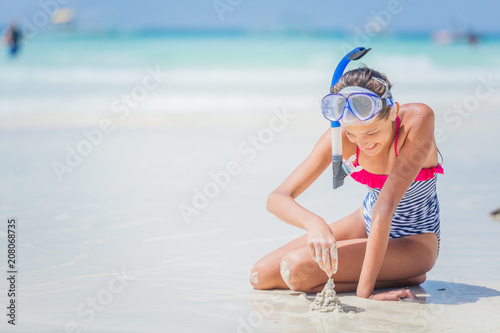 Girl in swimsuit and scuba mask sitting and having fun on tropical beach