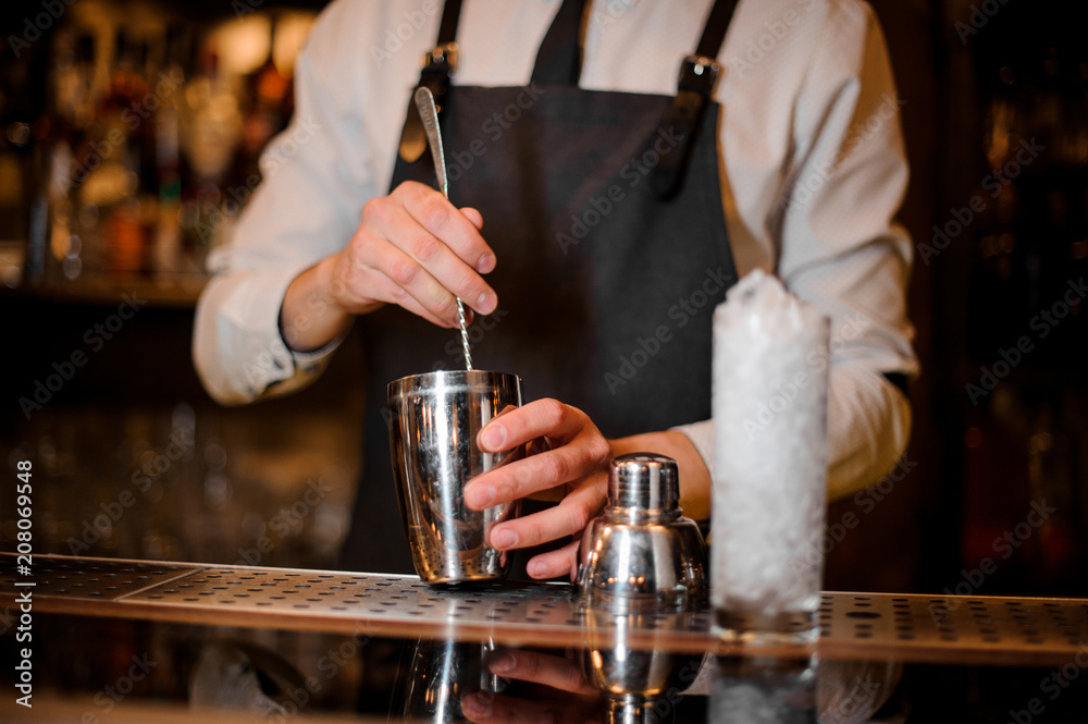 Bartender stirring an alcoholic drink in the steel shaker