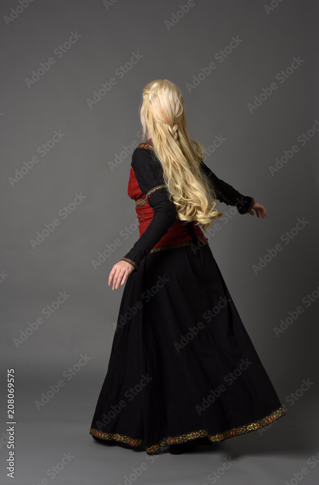 full length portrait of pretty blonde lady wearing a red and black fantasy medieval gown. standing pose on grey background. full length portrait of pretty blonde lady wearing a red and black fantasy medieval gown. standing pose on grey background.