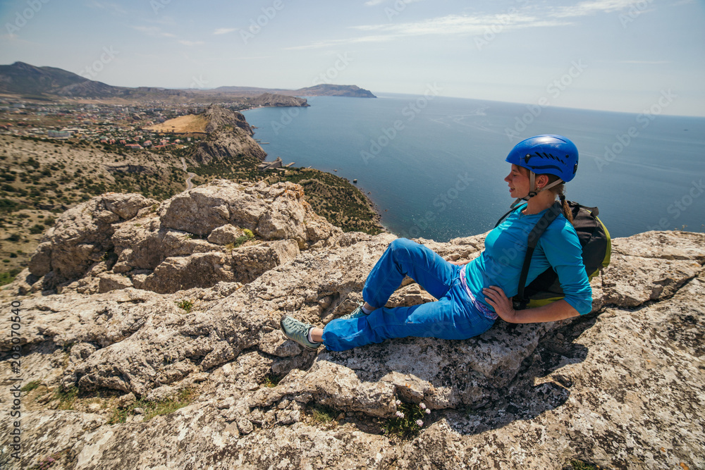 A girl in a helmet sits on the top of mountain 