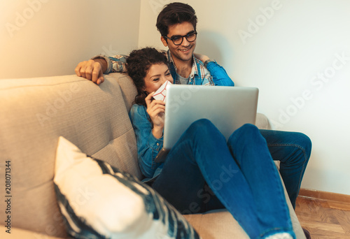 Smiling young couple sitting on sofa at home enjoying together, shopping online over the laptop. © Zoran Zeremski
