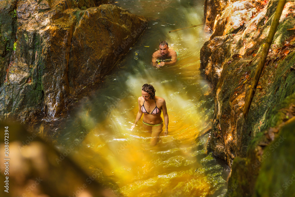 Fototapeta premium Man with action camera records his girlfriend swimming in a waterfall pool