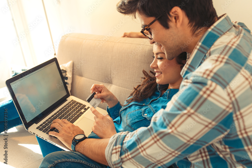 Smiling young couple sitting on sofa at home enjoying together, shopping online over the laptop. Smiling young couple sitting on sofa at home enjoying together, shopping online over the laptop.