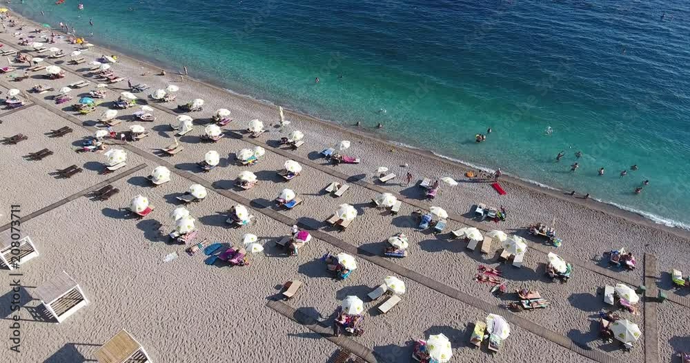 Flying over the beach with its umbrellas and people who sunbathe and swim in the clear blue sea water Flying over the beach with its umbrellas and people who sunbathe and swim in the clear blue sea water