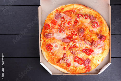 Pizza on a black wooden background, Italian pizza with tomatoes, bacon, sausages and cheese, fast food, festive food on a dark background, copy space, American cuisine