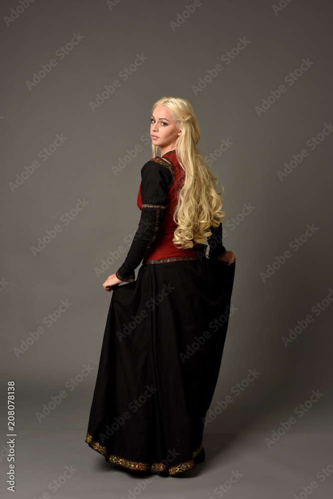 full length portrait of pretty blonde lady wearing a red and black fantasy medieval gown. standing pose on grey background. full length portrait of pretty blonde lady wearing a red and black fantasy medieval gown. standing pose on grey background.