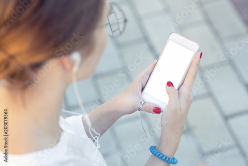 Template of a close up on a woman's hands, holding a phone while wearing headphones. Communicate inside the copy space about phone applications, music listening, street style, youth