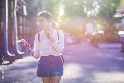 a beautiful young woman in alternative style wearing glasses, is using an application in her smart phone device. Communicate about youth, street style, spring, summer, phone, technology, applications.