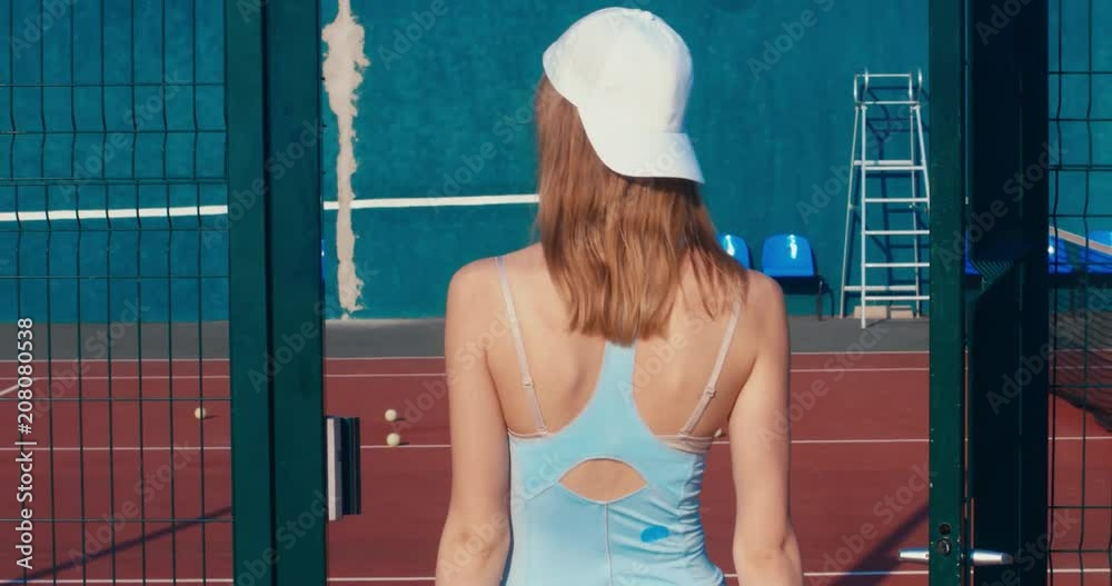 Portrait of young Caucasian teen model wearing fashionable tennis dress, walking on tennis hardcourt, summer sunny day outdoors. Fashion portrait shoot