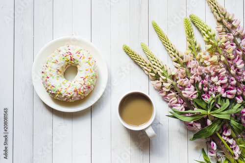 Still life with a Cup of coffee and lupine flowers donut on a light wooden table. Copy space