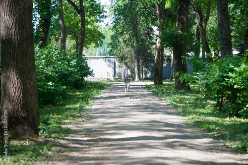 Blurred image of people walking in the park. A woman is walking with a dog. A child is riding a bicycle