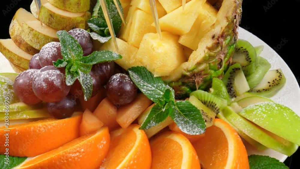 Mixed fruits plate, sliced pineapple, orange, kiwi, pear, apple and grapes, decorated with mint and icing sugar Mixed fruits plate, sliced pineapple, orange, kiwi, pear, apple and grapes, decorated with mint and icing sugar