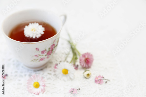 Cup of tea with daisies on white background