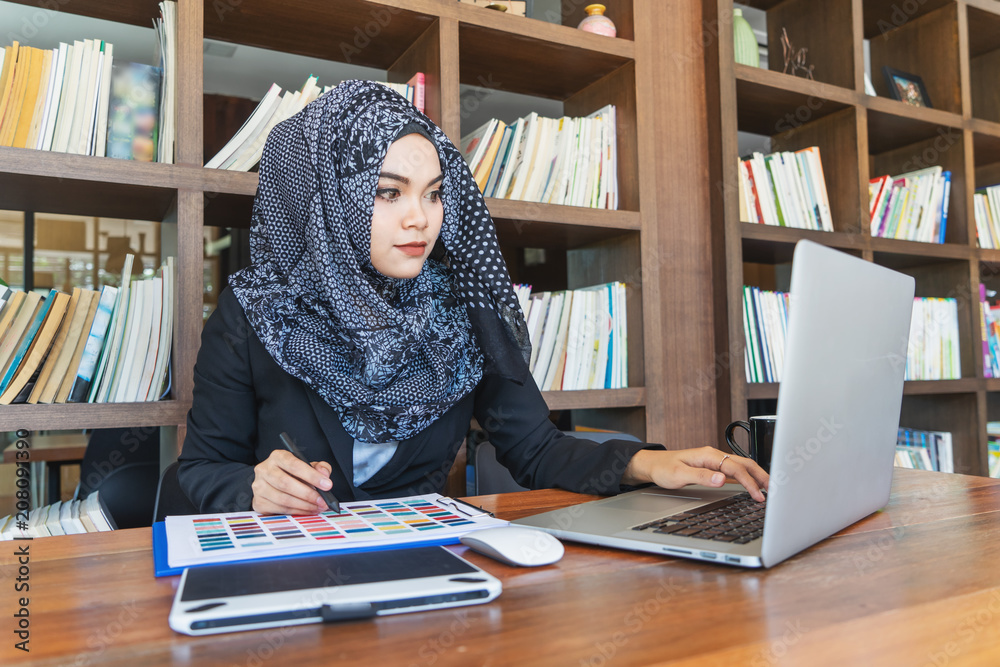 Young muslim asian female designer using graphics tablet while working with computer at studio or office. Young muslim asian female designer using graphics tablet while working with computer at studio or office.