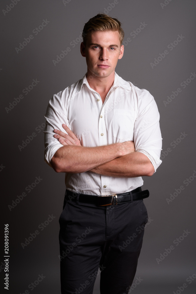 Young handsome businessman with blond hair against gray backgrou Young handsome businessman with blond hair against gray backgrou