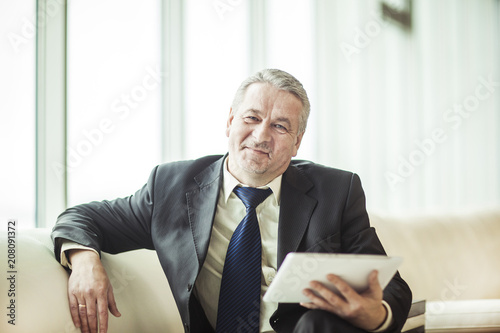 smiling experienced businessman with digital tablet sitting on sofa in the office