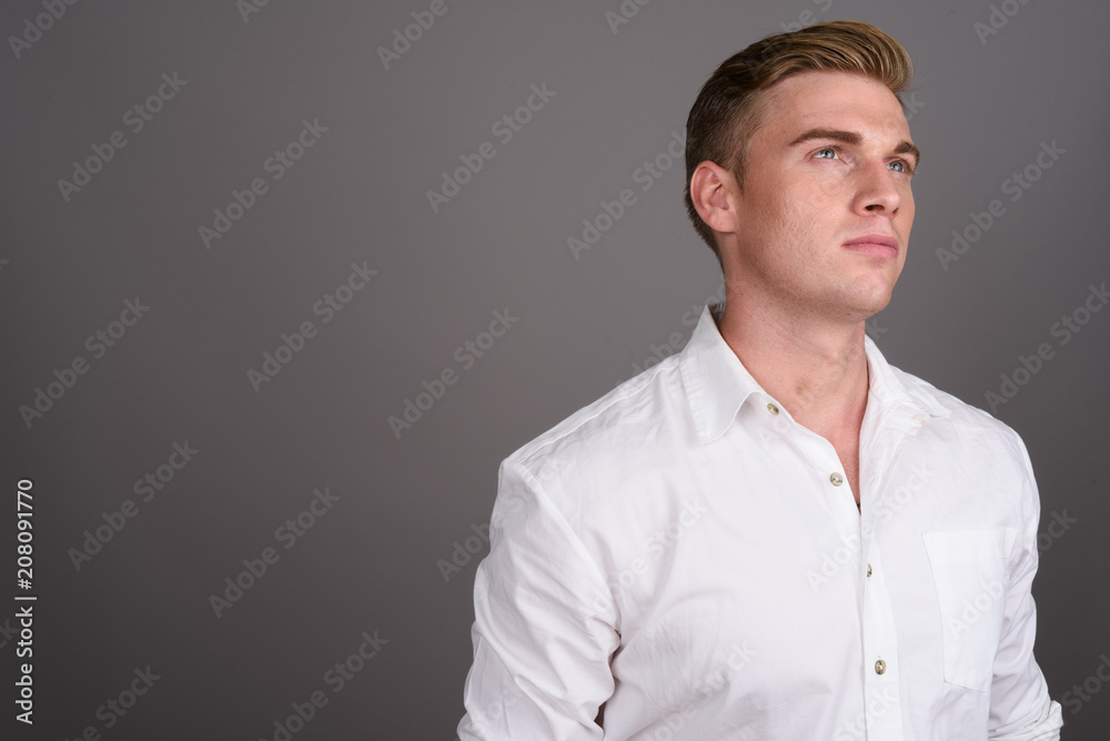Young handsome businessman with blond hair against gray backgrou Young handsome businessman with blond hair against gray backgrou