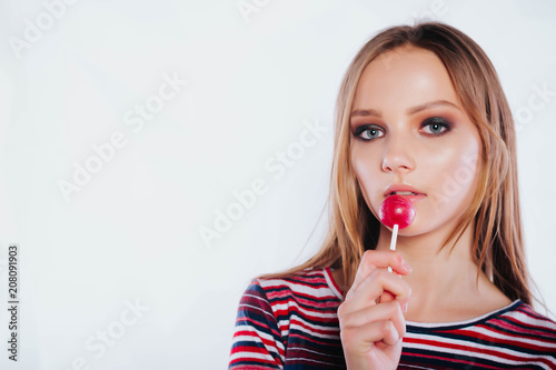 Beautiful girl licking a lollipop.Beautiful woman with creative makeup holding a candy, closeup portrait