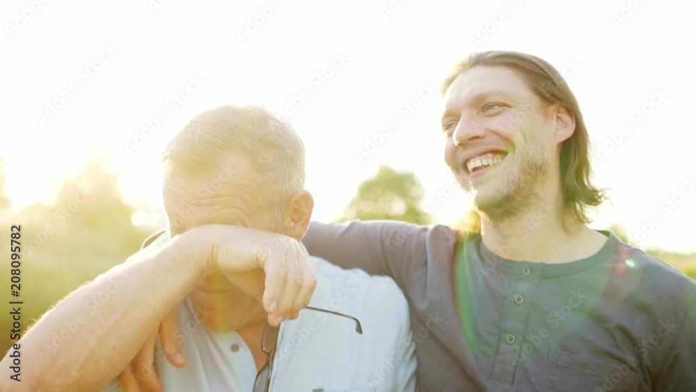 Father and son have a good time on the river bank. Evening sunset. The men talk and laugh. Father takes off his glasses and rubs his eyes. Fathers day