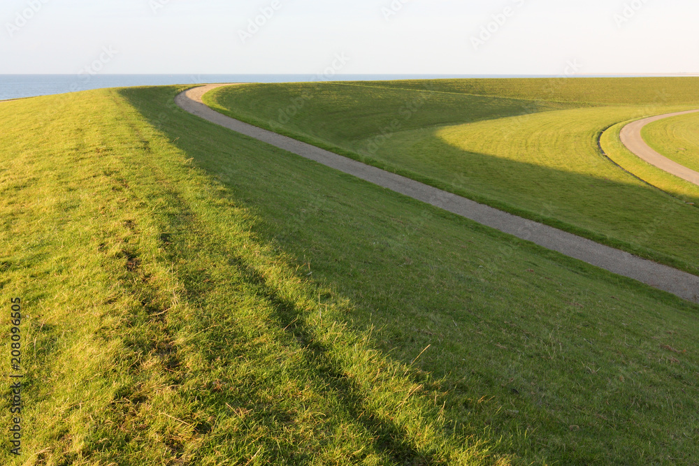 Curved sea dike with green grass and strong light and shadow near the Wadden Sea in Friesland, The Netherlands