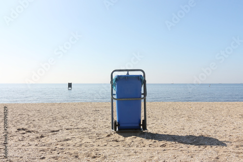 Blue trash bin on a sunny beach with a blue sea and blue sky