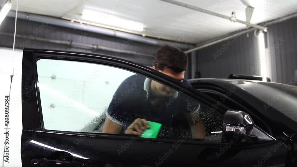 Master installs tint film for car glass with hairdryer and spatula with glare of light. Concept tinting Master installs tint film for car glass with hairdryer and spatula with glare of light. Concept tinting
