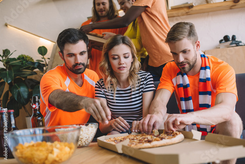 group of friends taking pizza slices from box on table at home photo